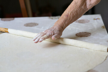 close up of grandmother's old wrinkled hands rolling dough with a rolling pin. Elderly woman rolling out dough with a rolling pin