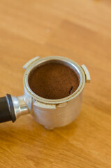 Freshly ground coffee overflowing over the rim of a metal filter on wood.High quality photo