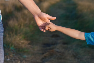 A Hands of a happy child and parent in nature in a park by the road