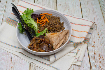 Vegan Indian bowl consisting of cooked lentils, flat bread, eggplant curry and salad