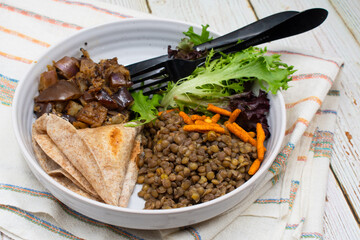 Vegan Indian bowl consisting of cooked lentils, flat bread, eggplant curry and salad