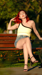 A beautiful red-haired young woman modeling stylishly in a wooded area on a summer day, giving chic poses in her summer dress