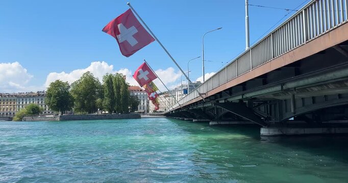 Swiss flag blows in the wind in Geneva at Mont Blanc Bridge at Lake Geneva on a sunny summer day