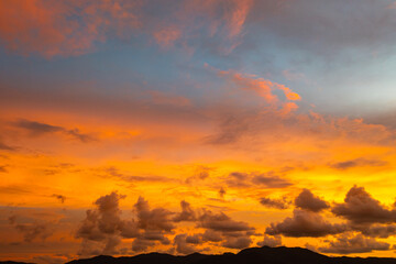 A breathtaking aerial view capturing a vibrant sunset over the Phuket countryside. The sky is ablaze with rich hues of yellow, orange, pink, and purple, while dramatic clouds float above the city