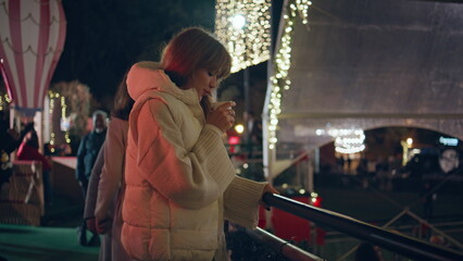 Fototapeta premium Woman enjoying drink fairground at night with Christmas lights. Happy girl park