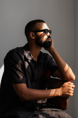 African american man in sunglasses and shirt sitting in sunlight on grey background