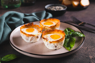 Chicken eggs baked in bacon and basil leaves on a plate on the table
