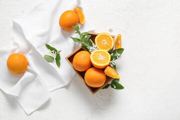 Wooden box of oranges with blooming branch on white table
