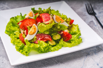 A light vegetable salad for healthy dietary nutrition. Tomatoes, cucumbers and boiled eggs with lettuce and traditional French vinaigrette sauce, on a white plate on a gray table.