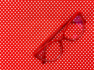 Pair of red cat eye shape women's glasses on a red polka dot background. Eye health concept.