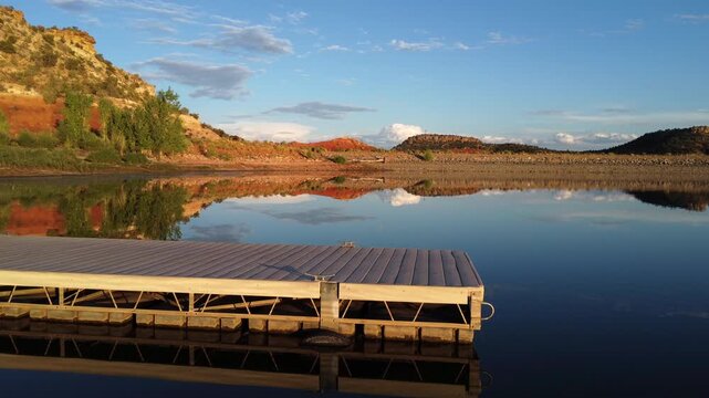 Discover the serene beauty of Escalante State Park in Utah through mesmerizing drone footage at golden hour. Tranquil flight over a lake dock with warm hues of the setting sun