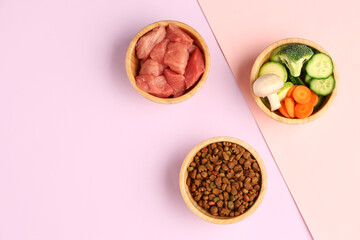 Bowls with dry pet food, raw meat and natural products on pink background