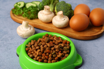 Bowl with dry pet food and natural products on color background, closeup