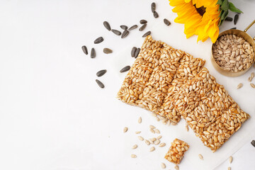 Tasty kozinaki with sunflower and measuring cup of seeds on white background