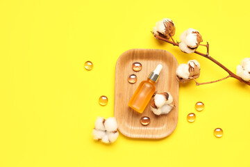 Composition with bottle of essential oil, glass stones and cotton flowers on yellow background