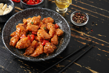 Tasty sweet and sour chicken in bowl with spices on dark wooden background, closeup