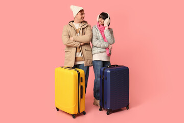 Beautiful young happy couple with suitcases on pink background. Winter vacation concept