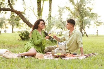 Beautiful young happy couple with glasses of wine having romantic picnic in park