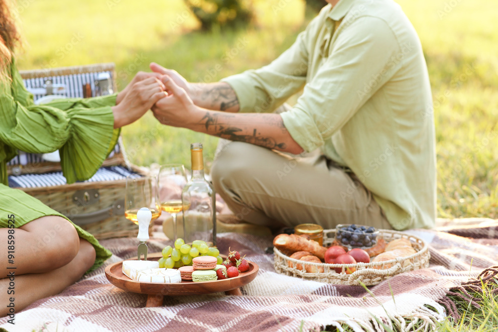 Poster Beautiful young couple with tasty food having on romantic picnic in park, closeup