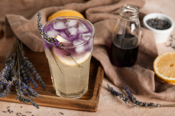 Wooden board with glass of cold lavender lemonade, syrup and flowers on color table