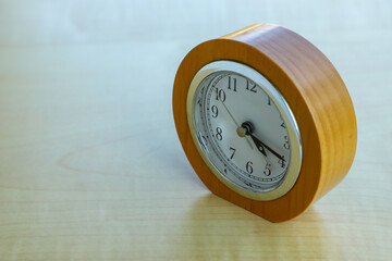 On a wooden textured light table there is a classic clock with a round dial, close-up. All in good...
