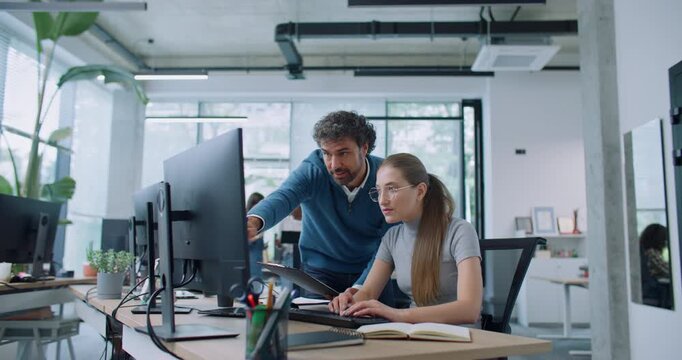 Attractive Caucasian leader controlling quality of work of his employee. Man comparing information on clipboard with data on computer. Busy woman typing text on keyboard while speaking with boss.