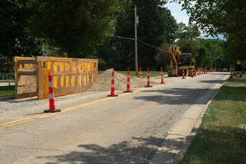 A trench box and excavator for water line replacement work on a city street with traffic cones for lane closure