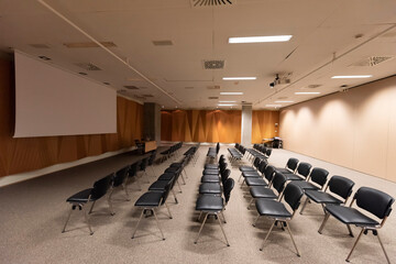 Large presentation screen in modern conference hall. Large presentation room with rows of chairs and a podium, ready for a corporate event