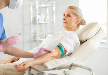 Obraz premium Old female patient lying on clinical chair having vein injection by young doctor