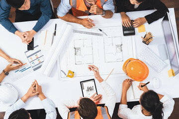 Top view banner of diverse group of civil engineer and client working together on architectural project, reviewing construction plan and building blueprint at meeting table. Prudent