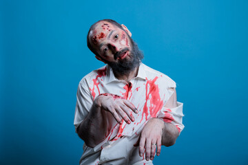 Man dressed as brainless zombie for Halloween event looking dumb and clueless. Person imitating mindless undead creature covered in blood and scars, isolated over studio background