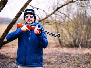A man in a blue jacket is holding a shotgun. The image has a mood of excitement and anticipation,...