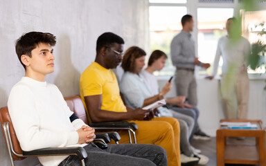 Young guy sitting in lobby of job center or employment office, waiting for interview or conversation with career counselor