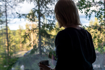 Naklejka premium blonde woman looking through the window on the forest in Rovaniemi Finland in summer time