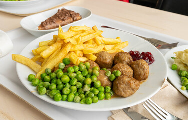 Meatballs with french fries, green peas, bechamel sauce and cranberry jam, meat balls on white plate