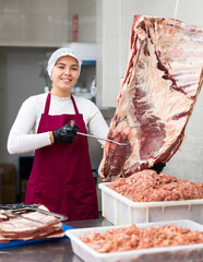 Young woman butcher in uniform hangs beef ribs on hook