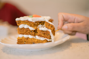 Woman eating delicious slice of carrot cake with fork in coffee shop