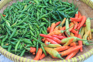 Red cayenne pepper and green cayenne pepper in a woven bamboo container on a wooden table

