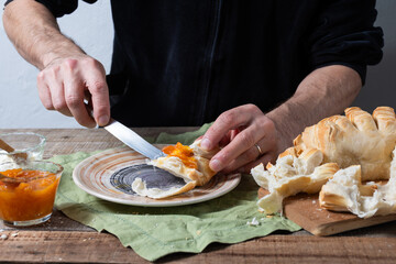 Hands spreading jam and cream cheese on a piece of bread.