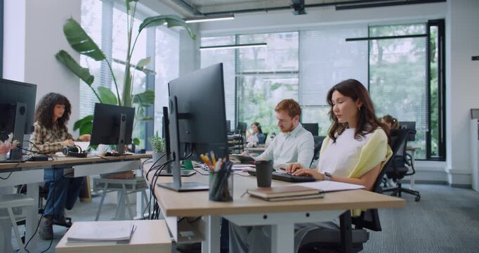 Camera view of busy mixed-raced managers working in large modern office. People sitting at desks with computers. Typing text on keyboards. Entering data on technology devices. Business concept.