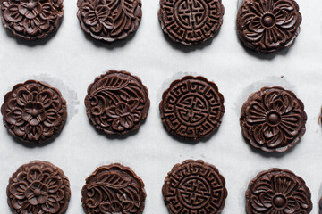 Overhead view of stamped chocolate cookies on a parchment lined baking tray, top view of embossed chocolate sugar cookies on a white background