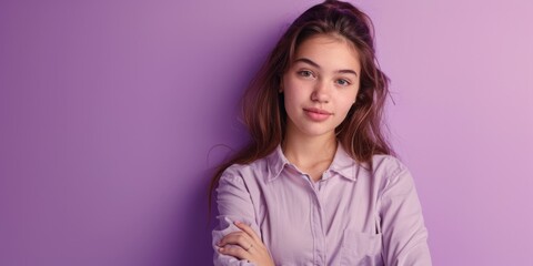 Fototapeta premium A woman stands with her arms crossed against a purple wall, conveying confidence and authority