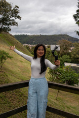 Latina woman visiting the city of Cuenca with the Pumapungo ruins in the background, using her phone to record herself while exploring the area