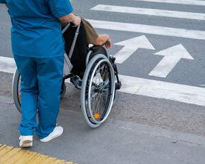 Rear view of a nurse helping an elderly woman in a wheelchair cross the road. 