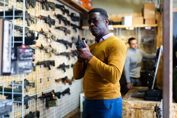 African-american man holding assault rifle in air weapon shop.