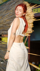 A beautiful red-haired young woman modeling stylishly in a wooded area on a summer day, giving chic poses in her summer dress