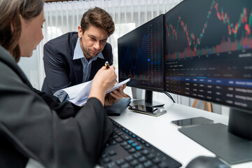 Two business traders discussing value business statistic graph company on paper report analyzing with dynamic stock exchange market currency real time website surround pc screens at office. Postulate.