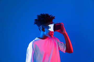 Surprised young African American looking through VR holding interesting object hologram on pink...