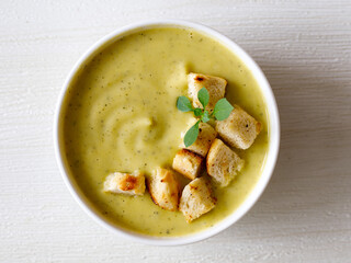 bowl of homemade zucchini cream soup with chicken and basil with croutons on white wooden table. Top view flat lay, close up