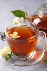 Hot jasmine tea in cup and flowers on light grey table